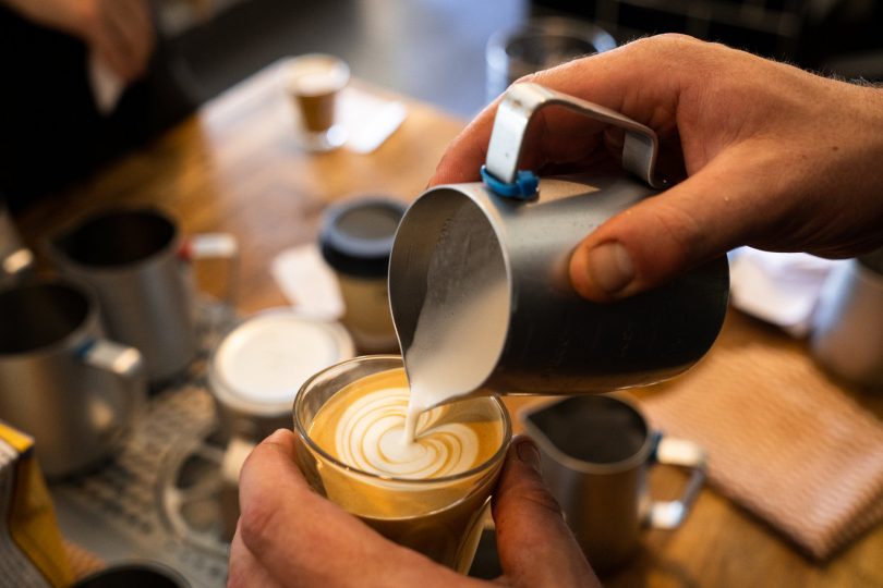 Man pouring frothed milk into latte.