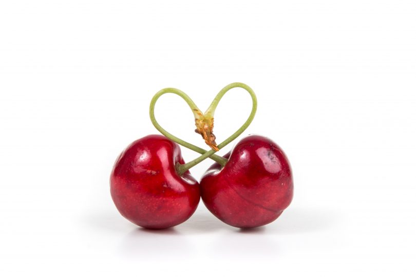 Two cherries tied together with stems forming love heart.