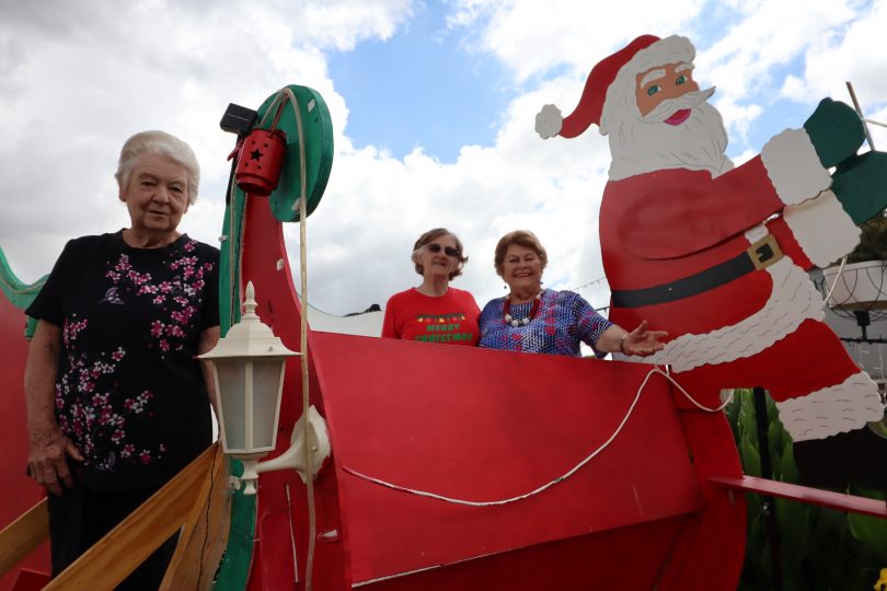 Freda Cook, Nancy Hook and Esma Drennan inside giant sleigh Christmas decoration.
