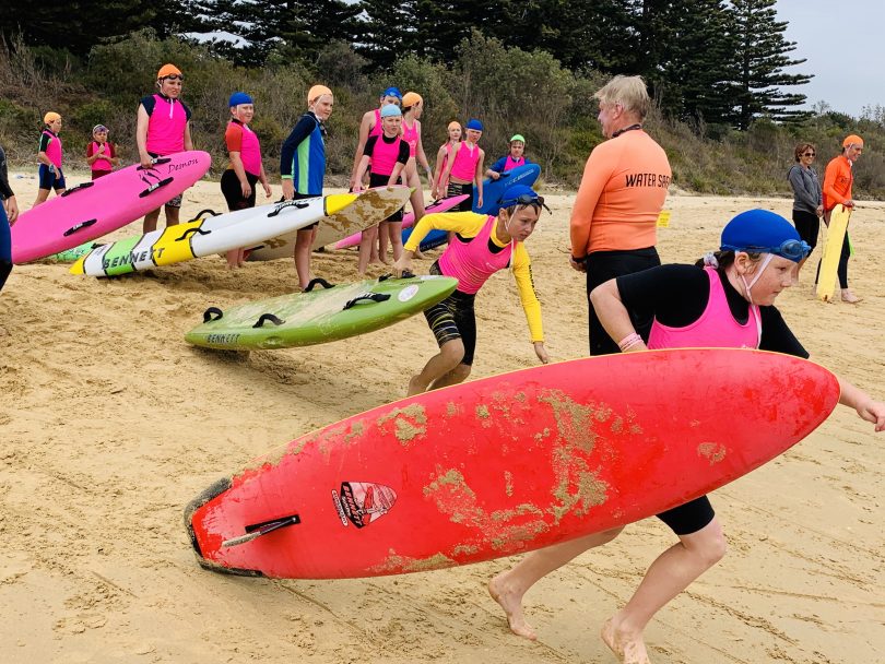 Young surf lifesavers on beach run towards the water with floatation devices.