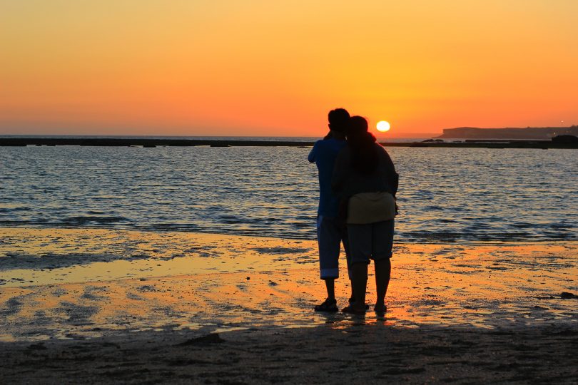 Romantic couple watching sunset on beach.