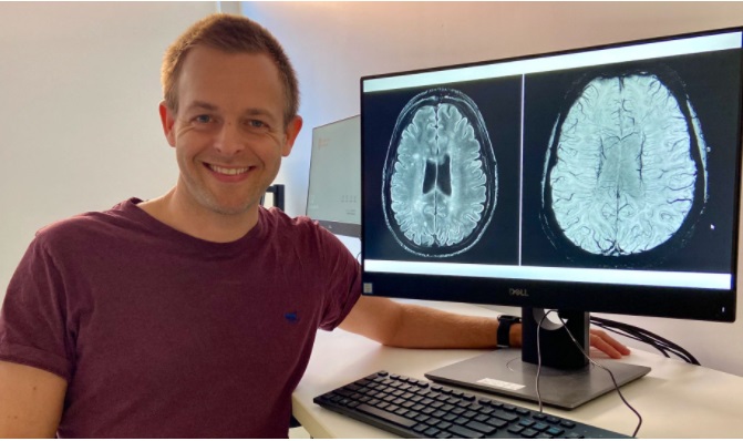 Johnathan Hewis with monitor showing MRI brain scans