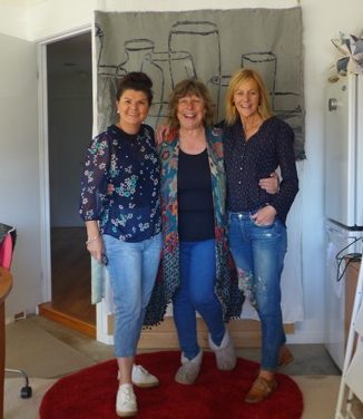 Three women in front of a textile artwork