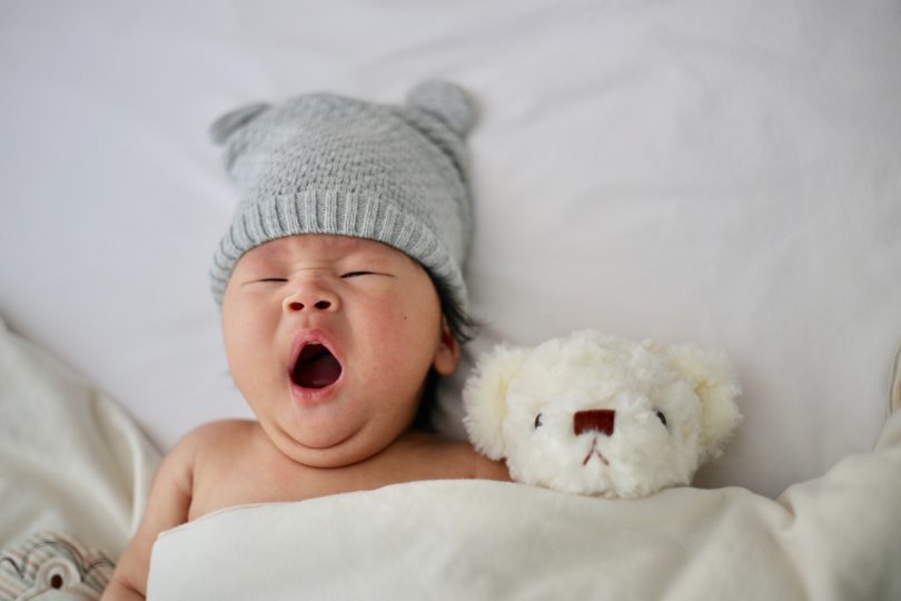 Baby in bed with teddy bear, yawning