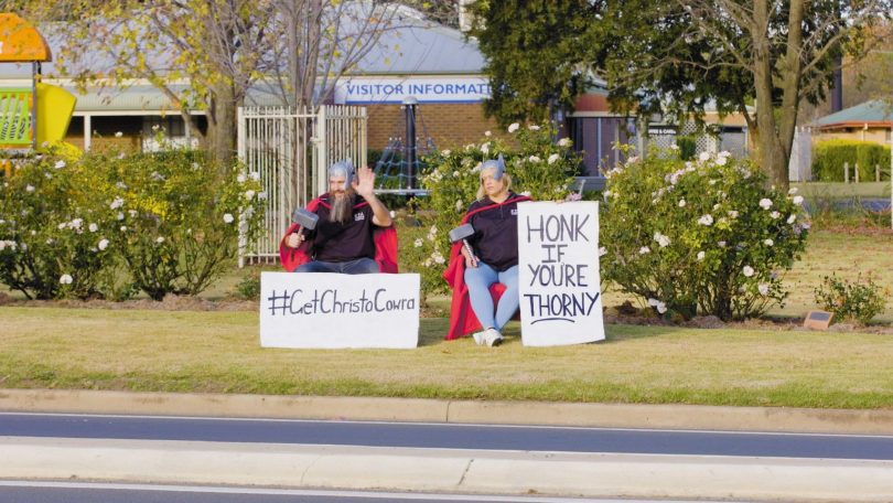 A still from Cowra tourism's #GetChrisToCowra campaign video of man and woman dressed as Thor sitting by roadside