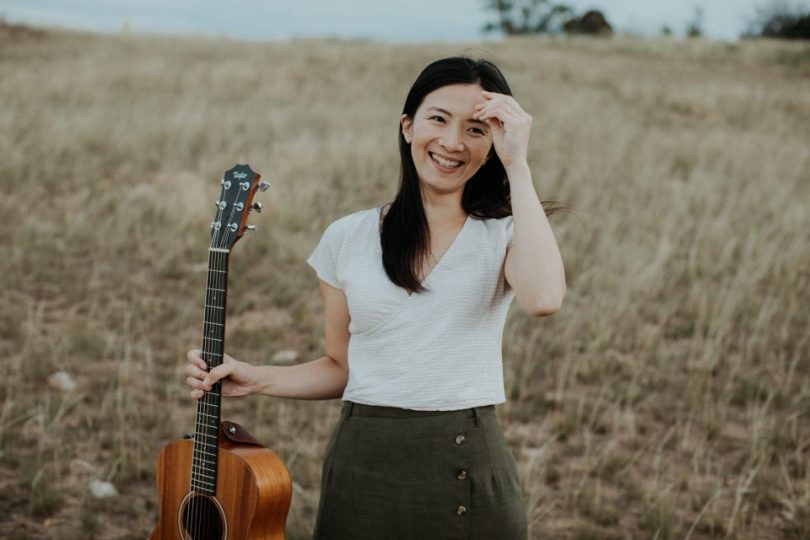 Kim Yang holding guitar in rural field