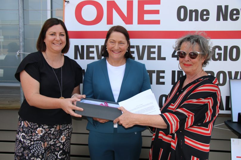 Cancer survivor Cathie Hurst (right) presents the ONE action group petition to Federal Member for Eden Monaro Kristy McBain and Federal Member for Gilmore Fiona Phillips.