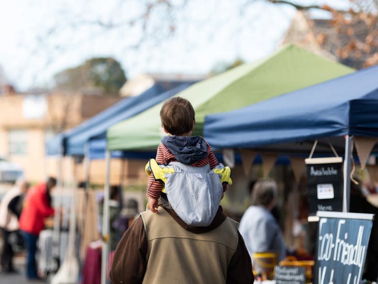 Child on adult's shoulders at market