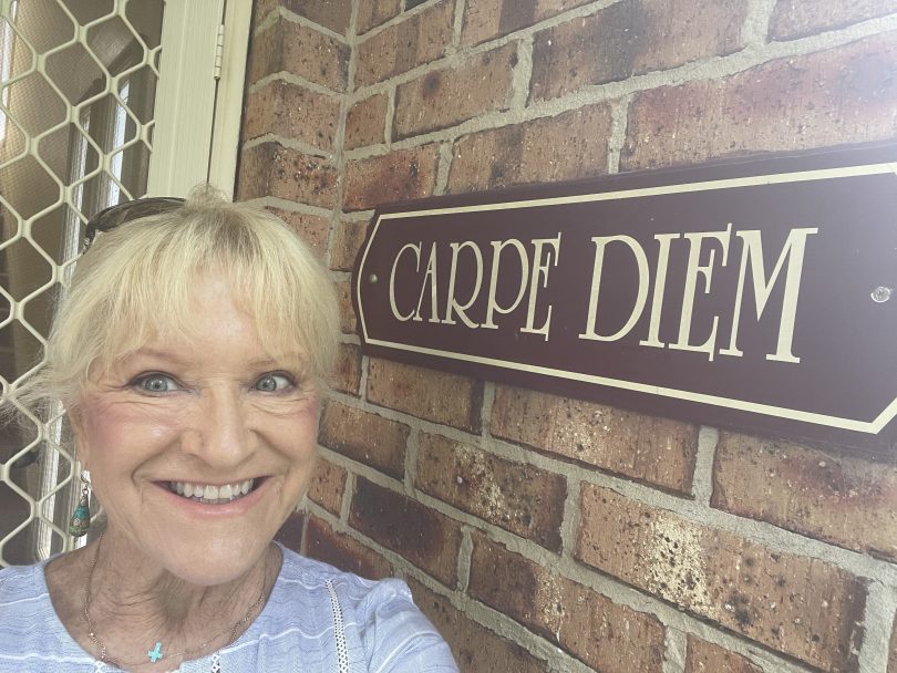 Woman outside her house with carpe diem on the wall.