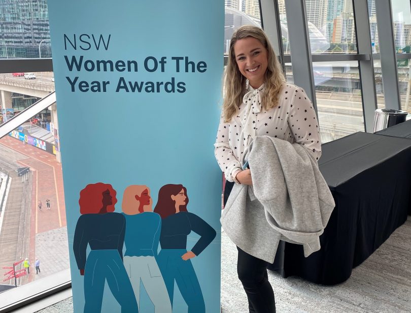 Woman standing next to NSW Woman of the Year Awards banner