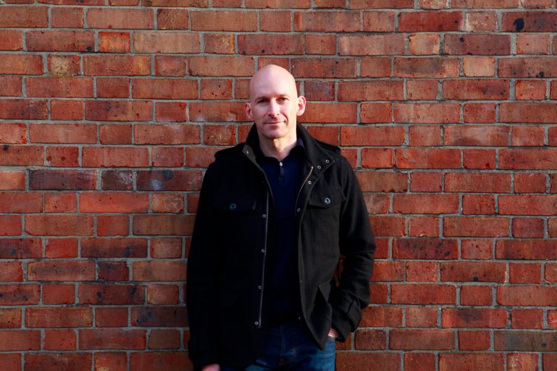 Author Andy Jones standing in front of brick wall