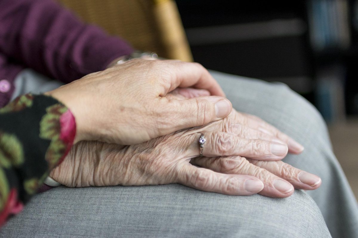 Younger hand resting on elderly person's hands.