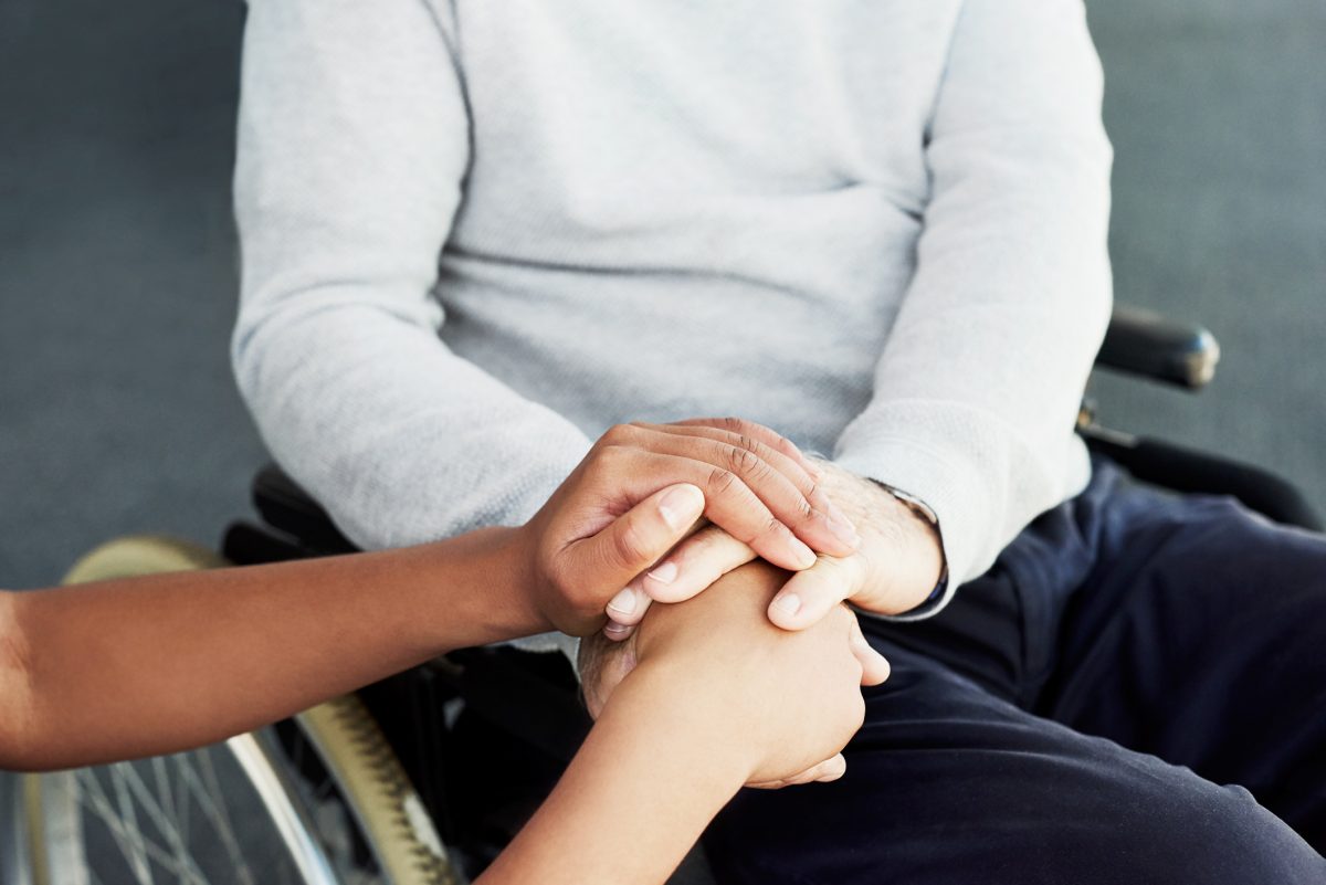 Carer holding the hands of a person in a wheelchair