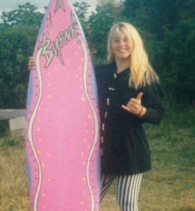 Priscilla Hensler with a pink surf board giving a thumbs up