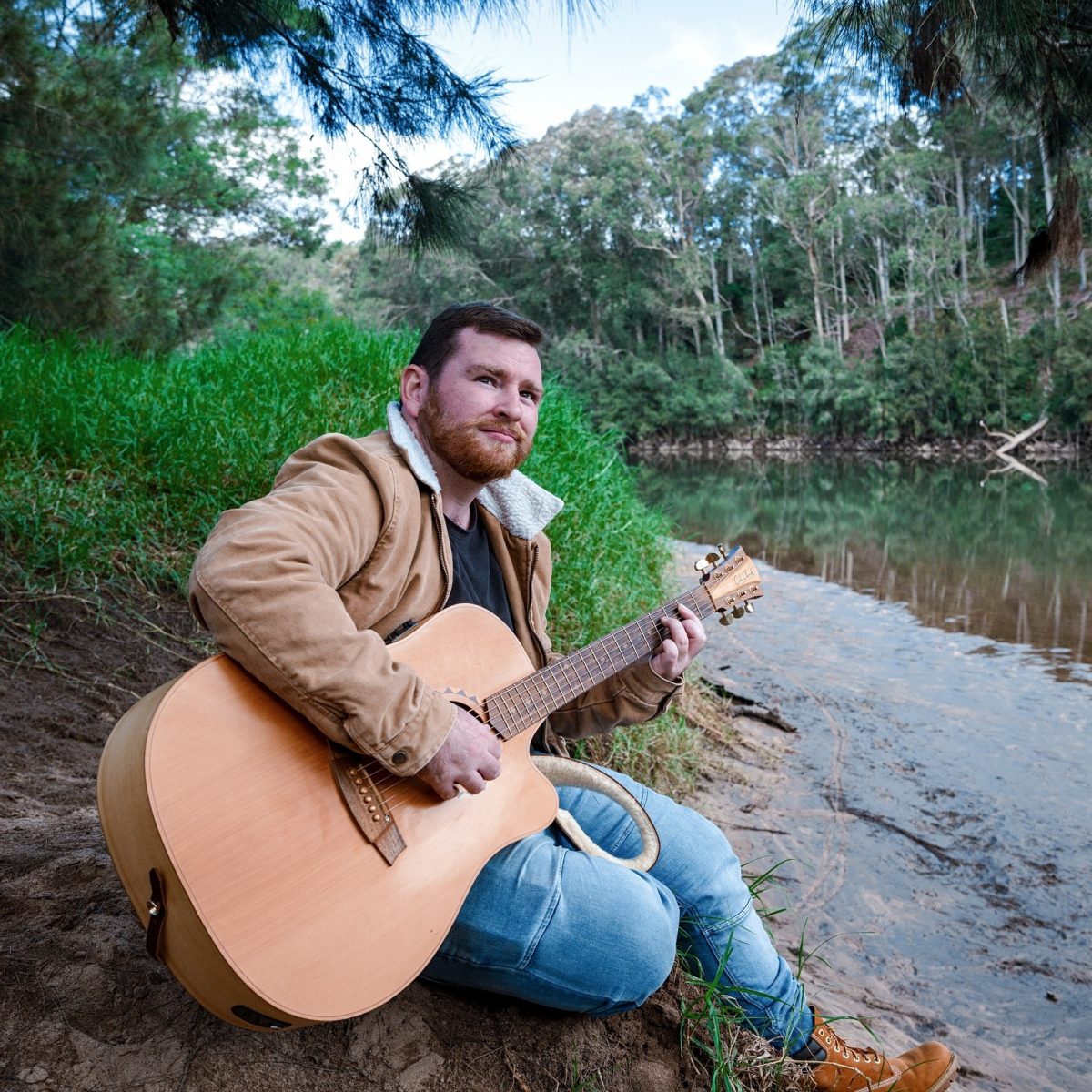 Ethan Parlato on a riverbank with his guitar