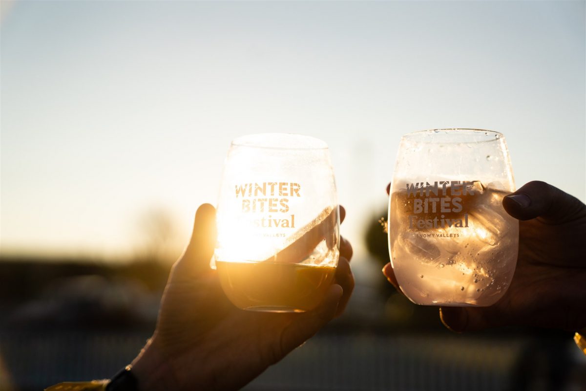 Hands holding two tumblers featuring Winter Bites logo in the sunset