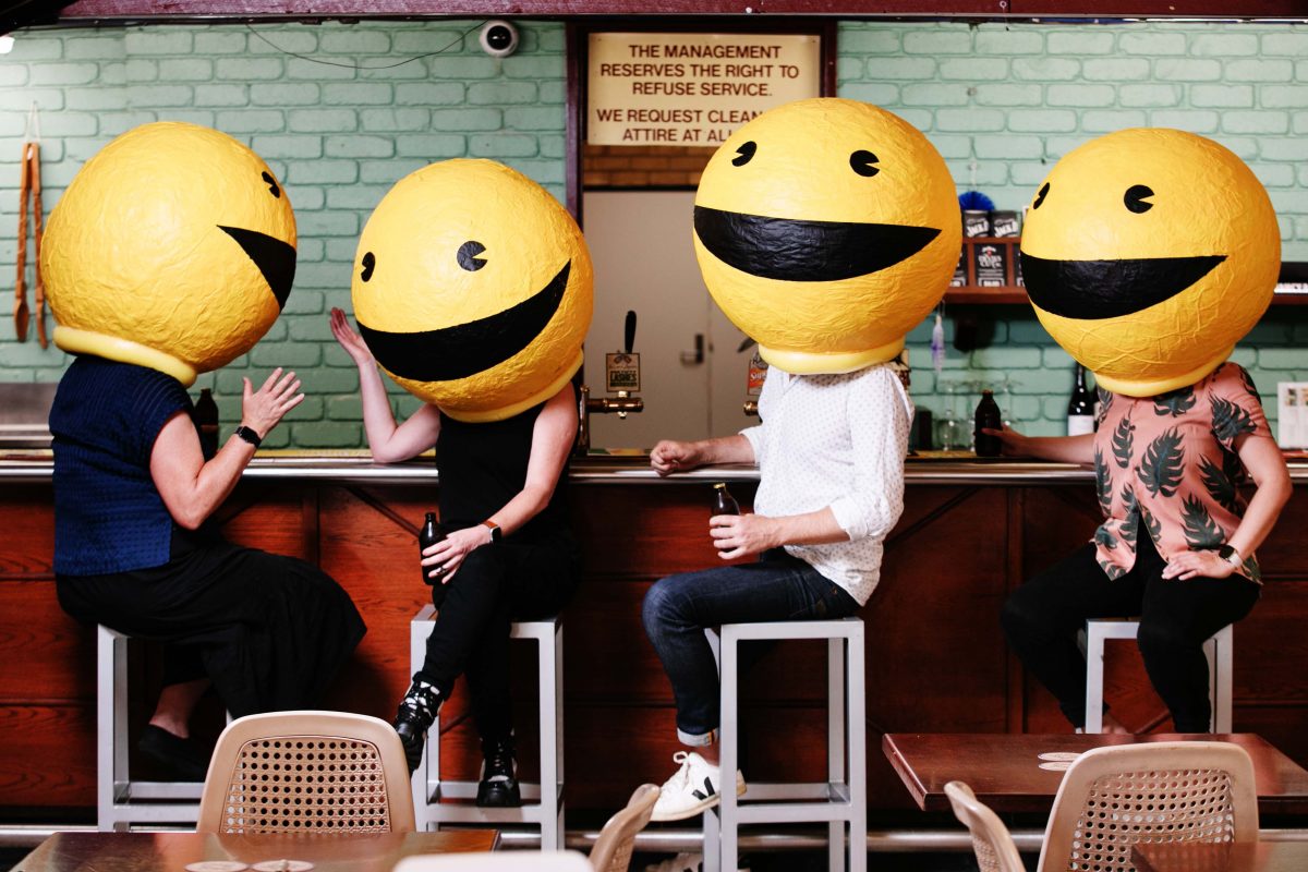 People sat at a bar with paper mache smiling faces on their heads