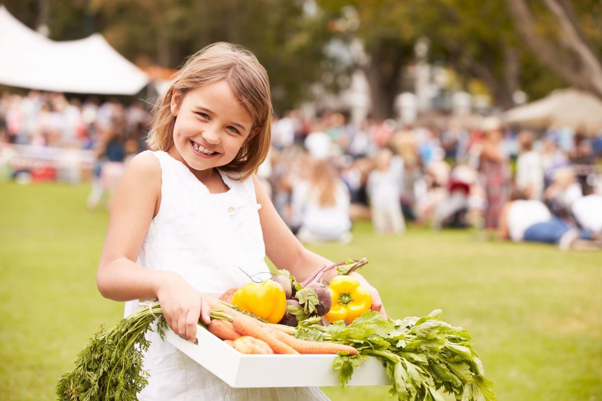 Smiling young girl in a white dress holding a box of vegetables