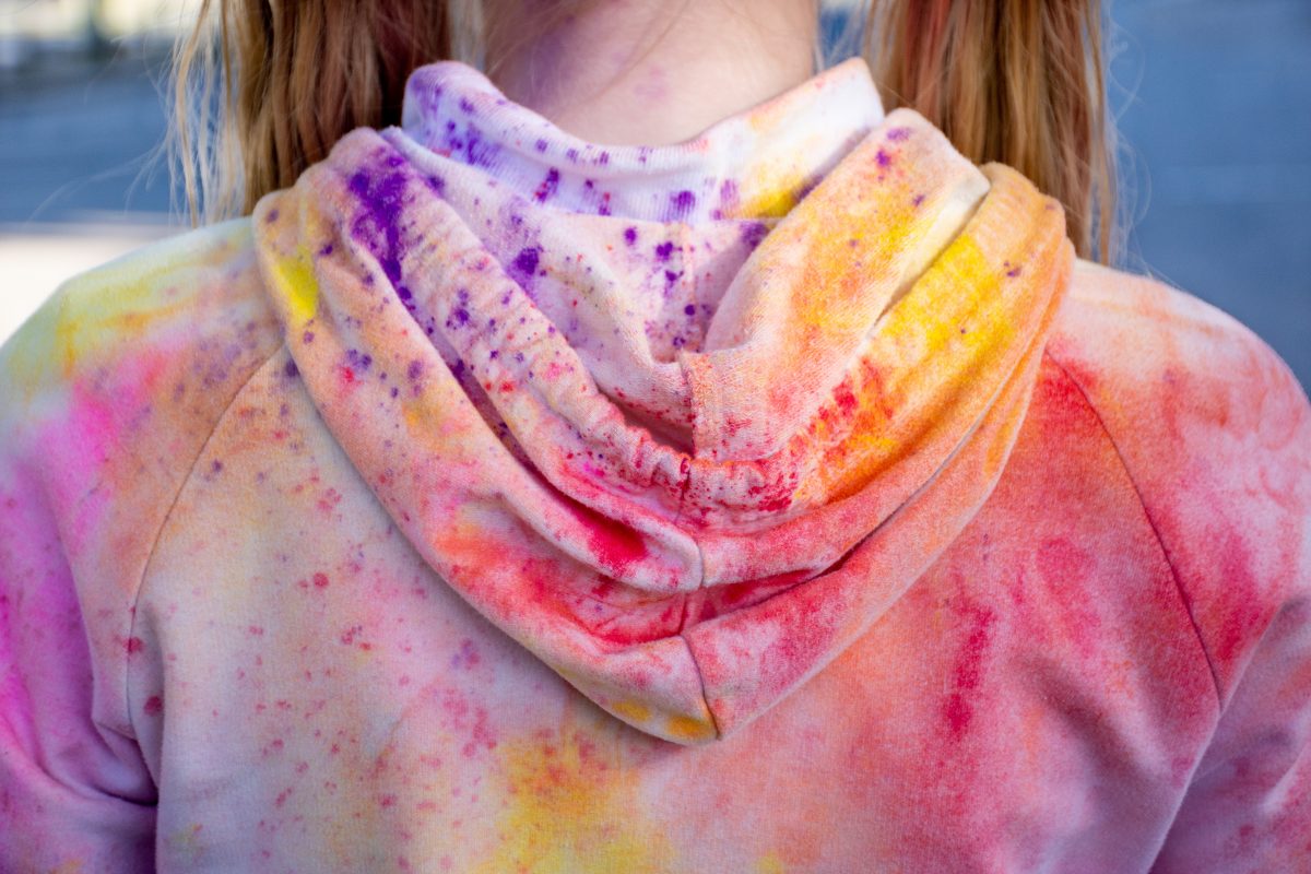 A child from behind wearing a white hoodie covered in multicoloured powder