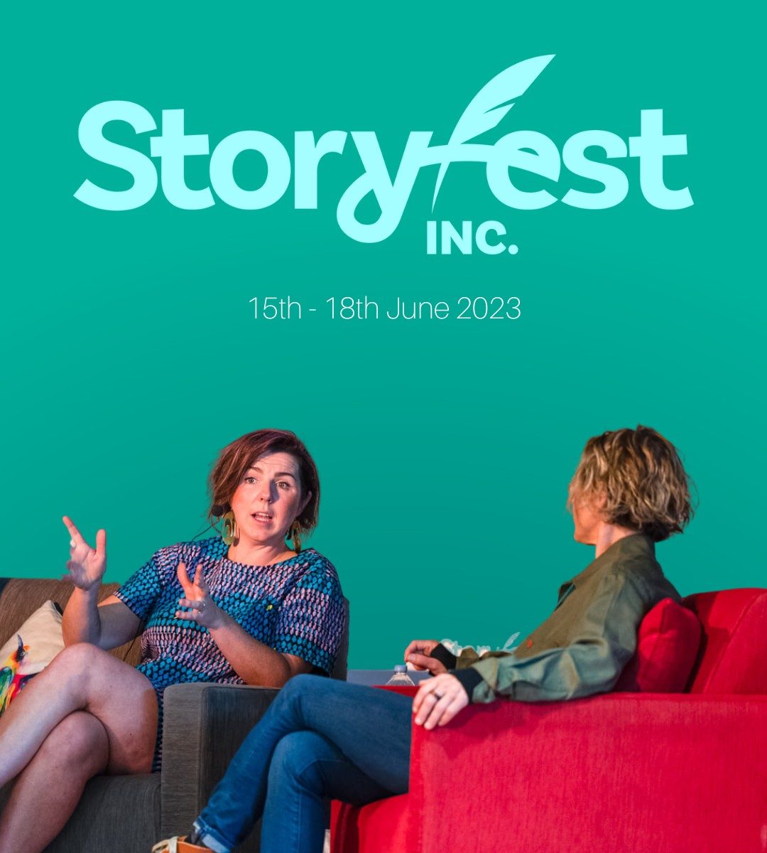 two women sitting down talking in front of the Storyfest sign