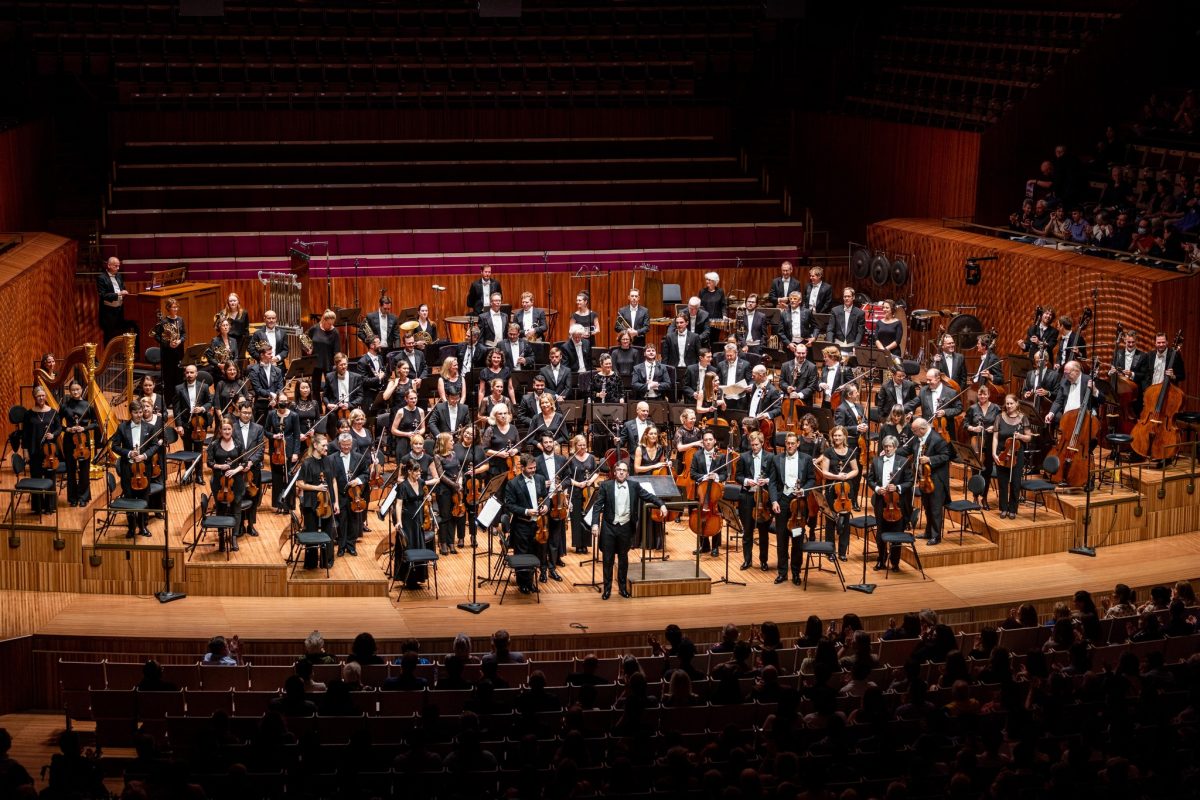 A photograph looking down at the Sydney Symphony Orchestra on the stage, standing with their instruments in hand