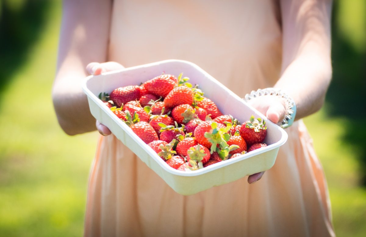 A woman holding a tray of strawberries in the sun. 