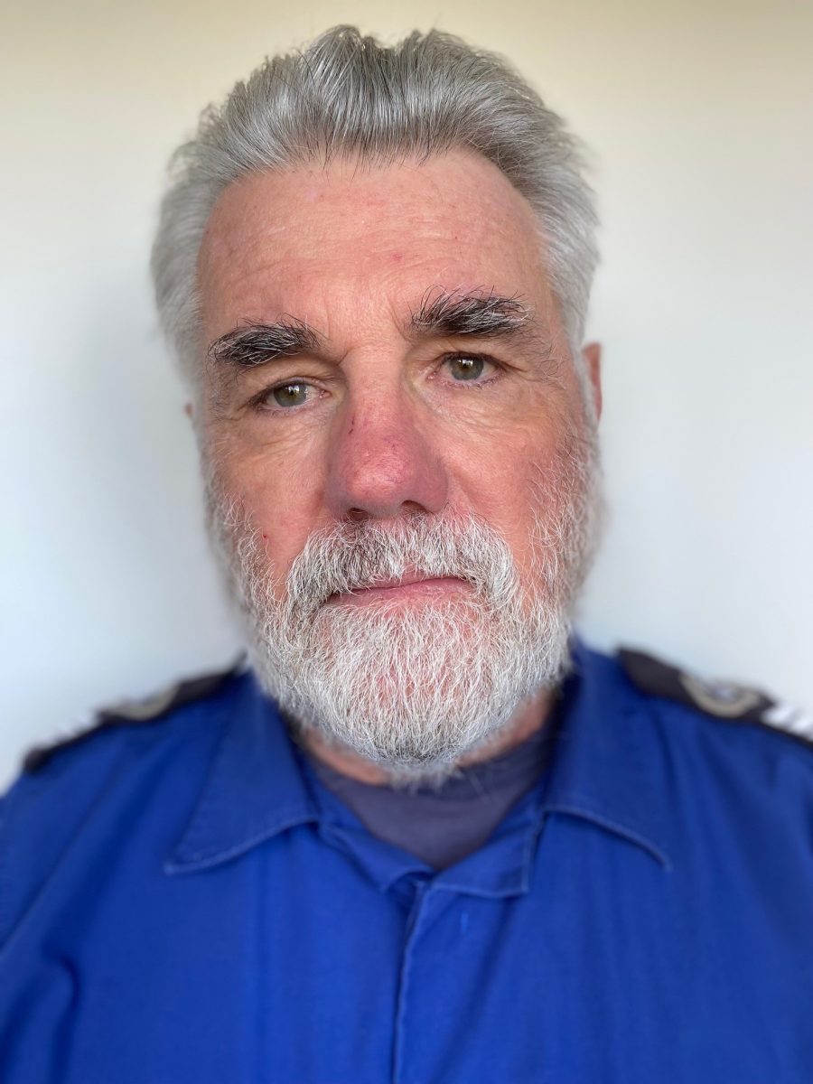 A middle aged white man with silver hair and white beard in a dark blue shirt