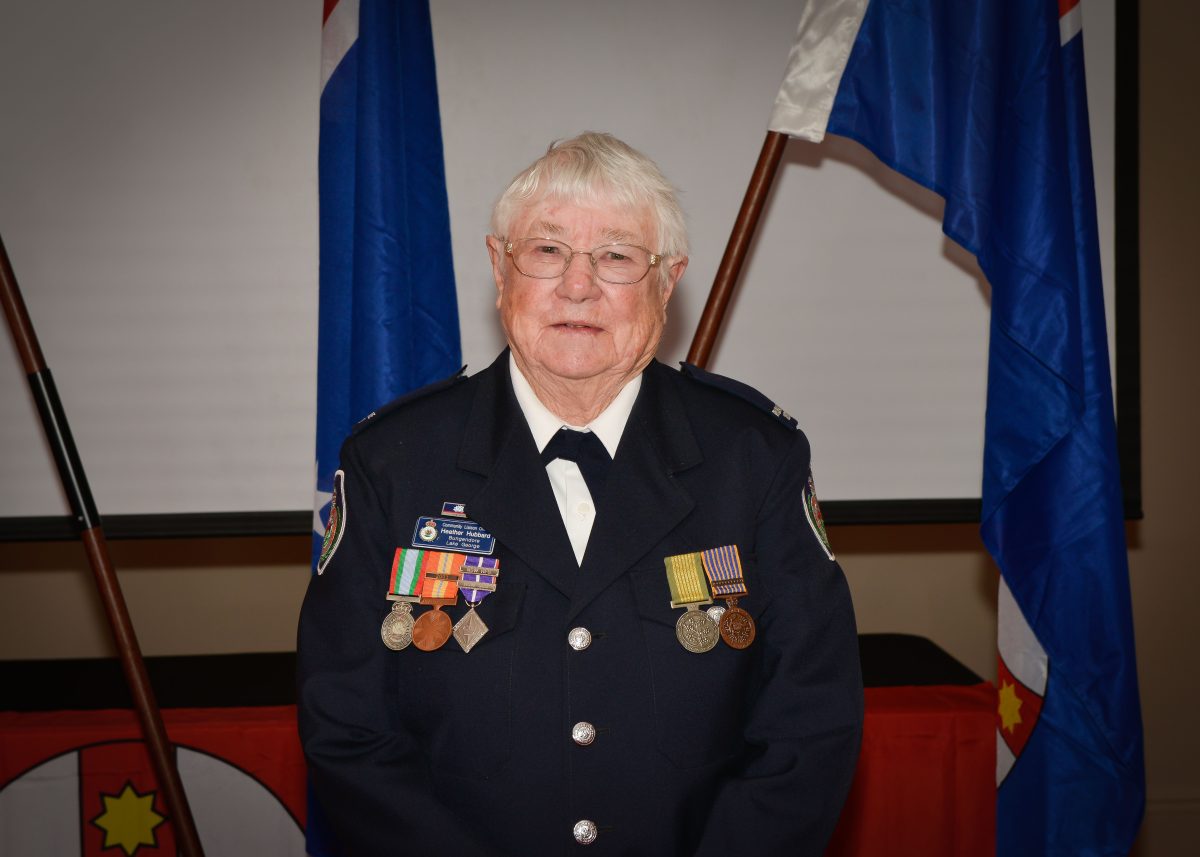 Portrait shot of a uniformed Heather standing in front of two flags.
