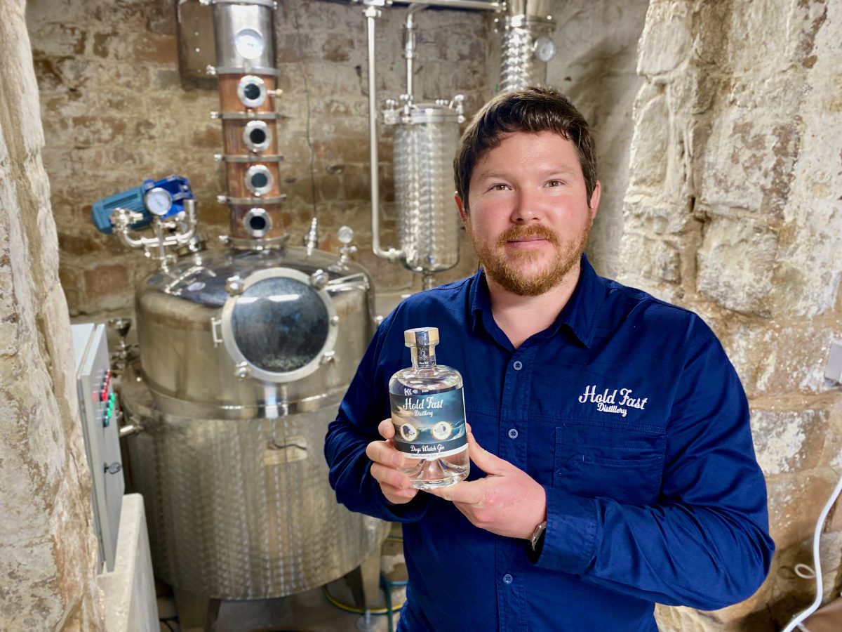 Gavin holds a bottle of gin in front of the still.