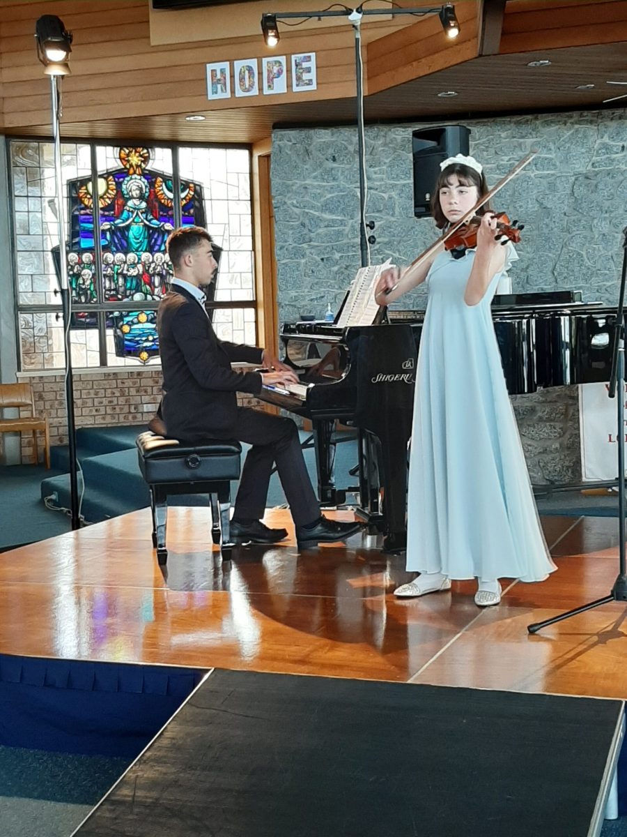 A young man in a suit on piano and a young woman playing violin in a teal dress