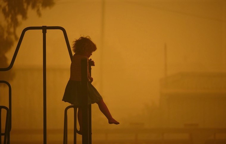 A young girl sitting on play equipment among an orange haze