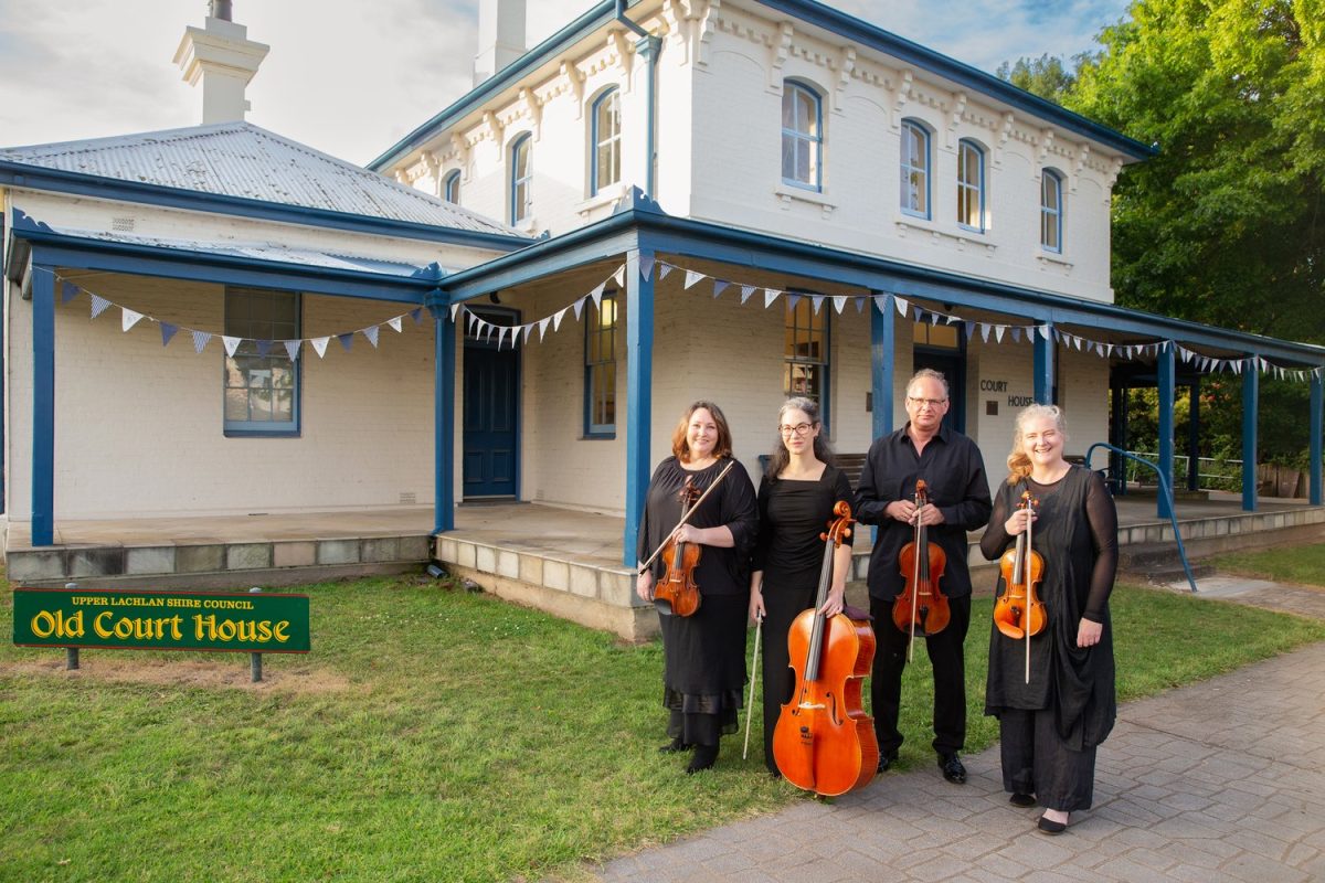 Four musicians standing with instruments in front of a building 