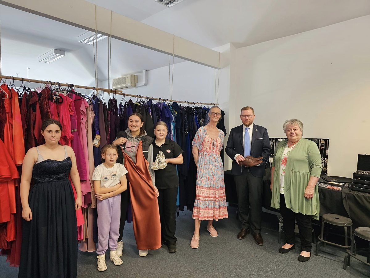 A group of people standing together in front of a clothes rack with formal dresses hanging from it