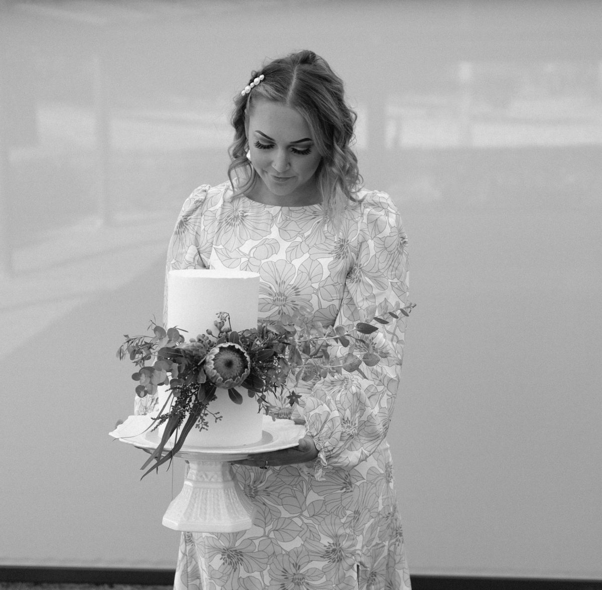 A black-and-white photo of a woman holding a cake and looking down
