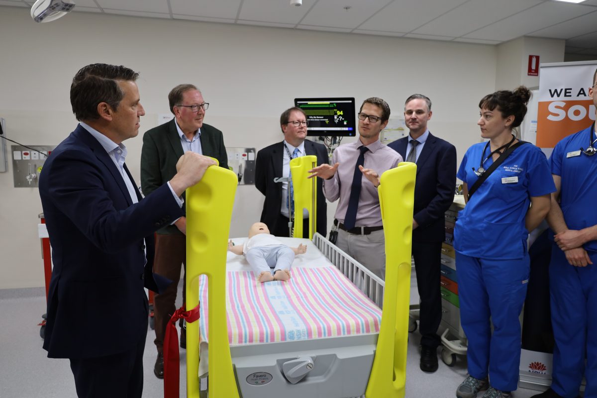 People standing around a hospital bed with a doll infant lying on its back