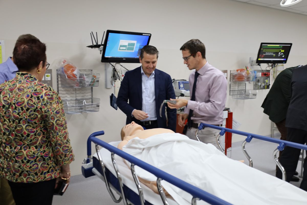 People standing around a hospital bed with an adult size mannequin 