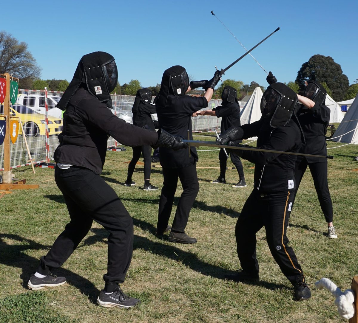 A group of people in black clothes and protective gear, fencing.