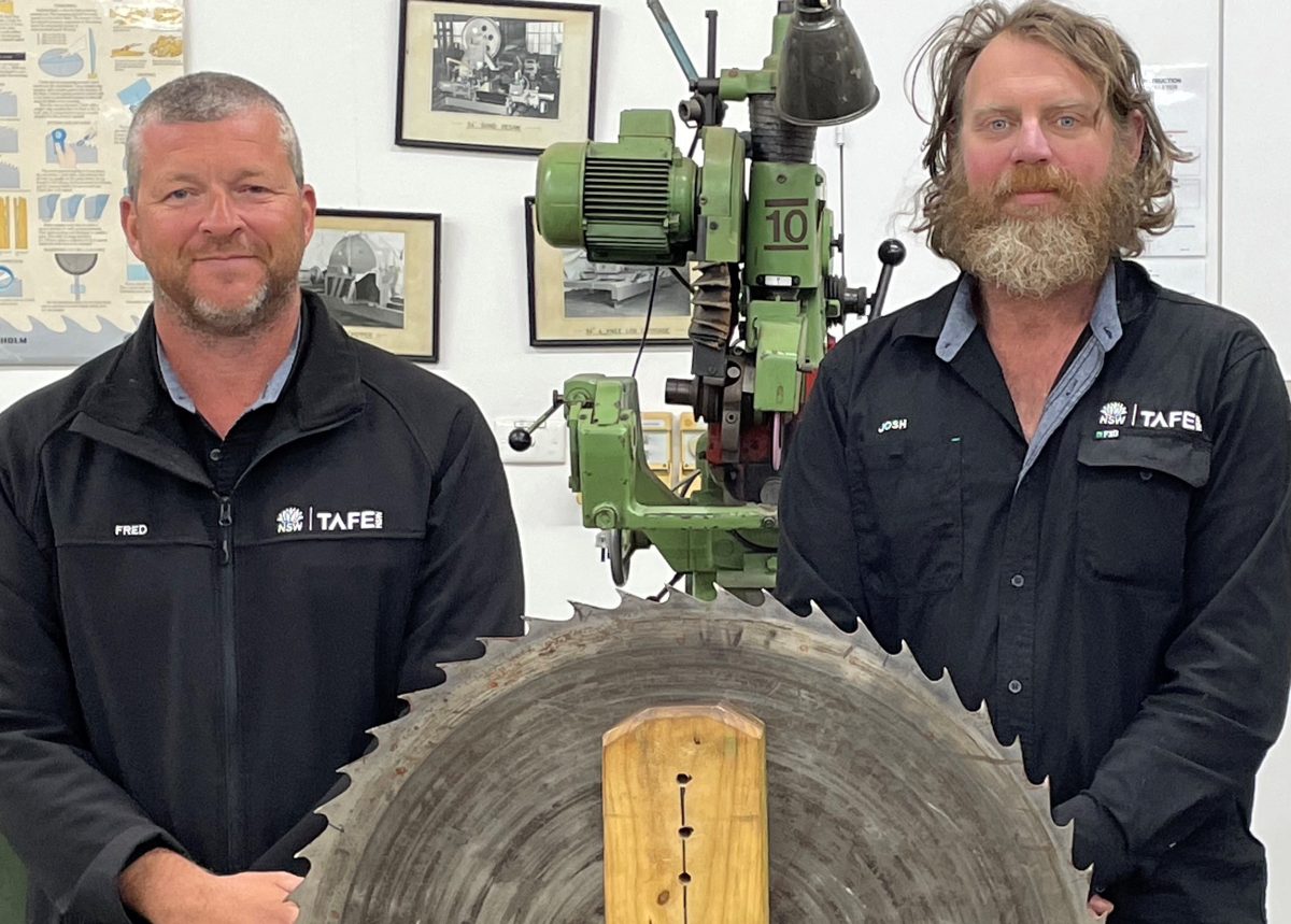 two men standing behind a giant timber saw