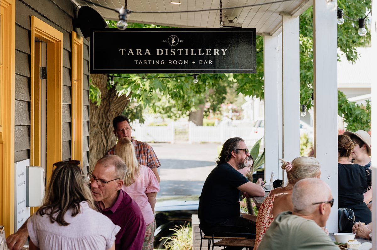 People drinking on a verandah with a sign for Tara Distillery hanging above