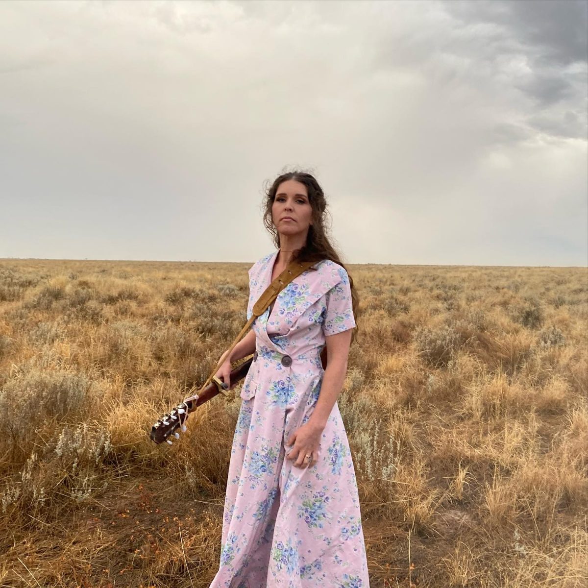a woman holding a guitar and standing in an open field
