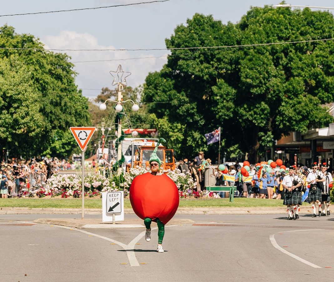 A man in a cherry costume at the head of a street parade