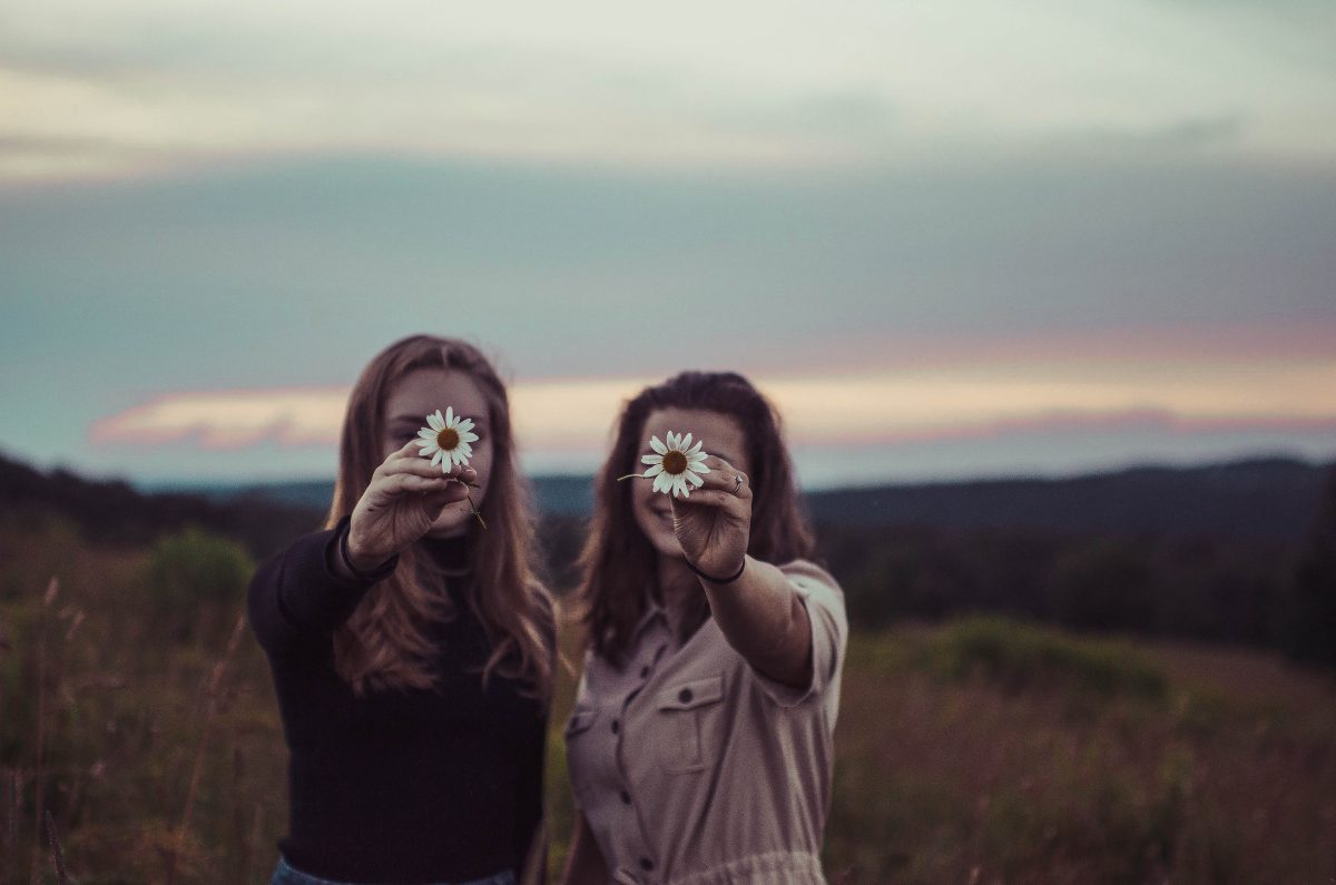 Two women in a field holding up sunflowers