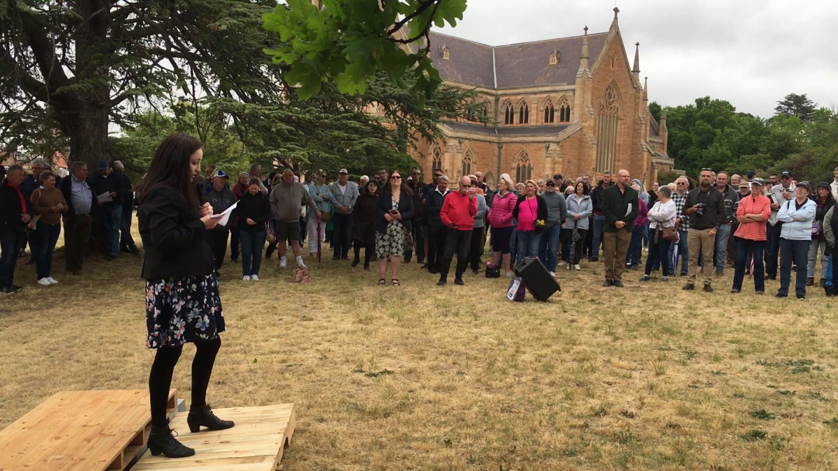 Woman standing on pedestal addressing crowd in front of church