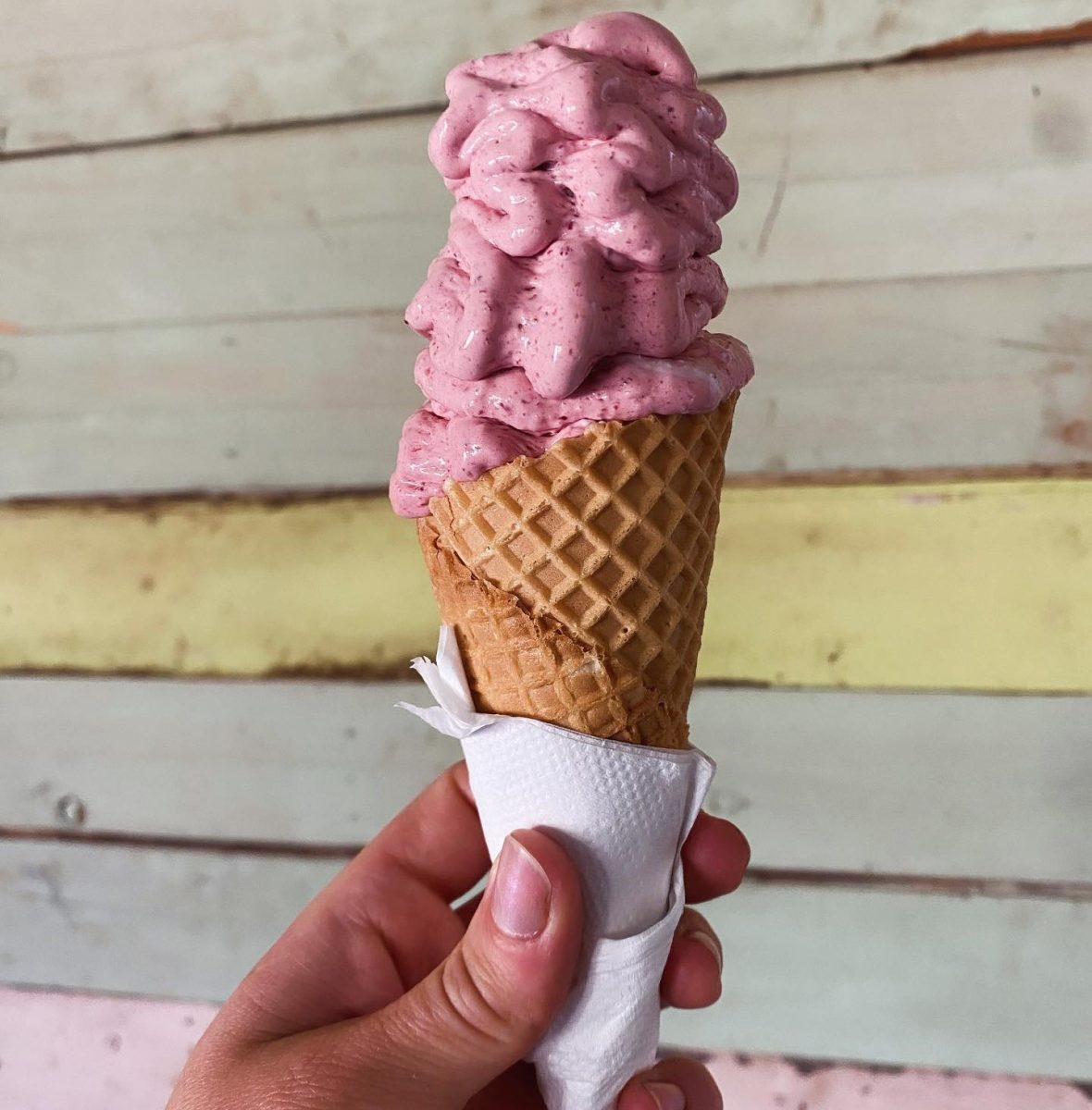 A hand holding a cherry ice-cream in cone