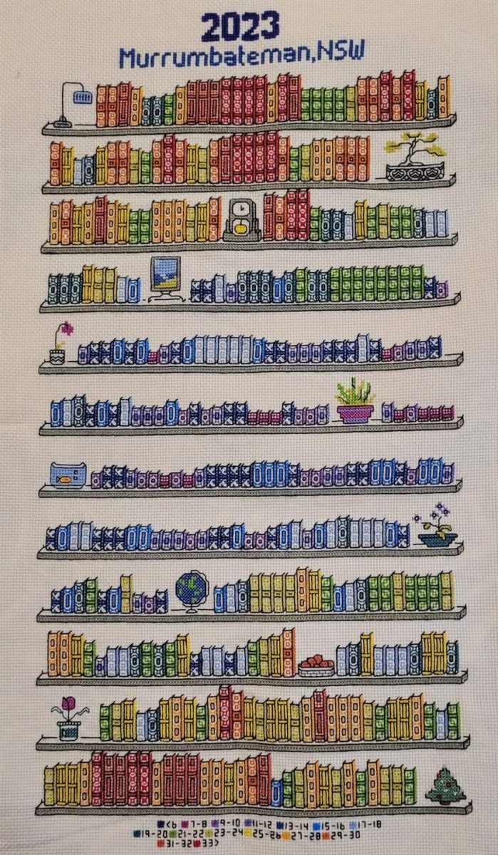 Cross-stitch work showing bookshelf with coloured books representing a year of weather in Murrumbateman. 