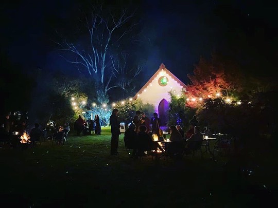 The venue at night and people standing around small firepits
