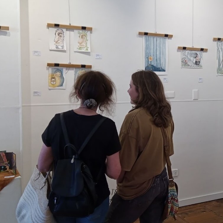 Two women looking at artworks hanging on a white wall