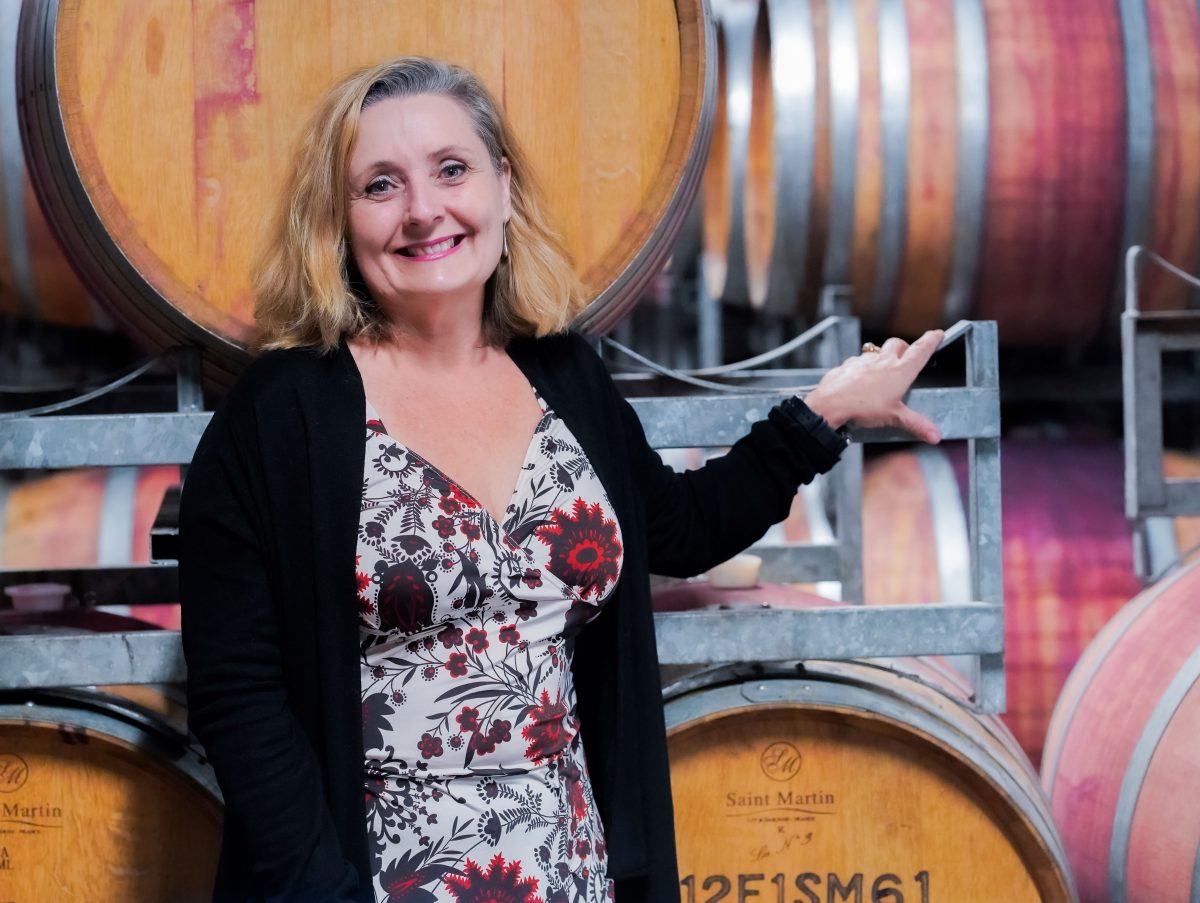 A woman stands in front of wooden wine barrels