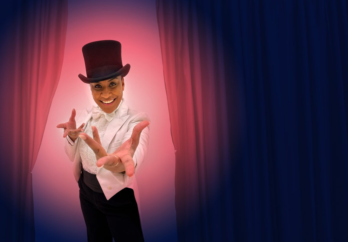 A woman in a top hat and suit in front of red curtains