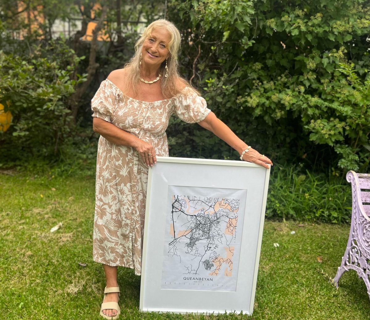 A woman in a dress posing next to a framed tea towel